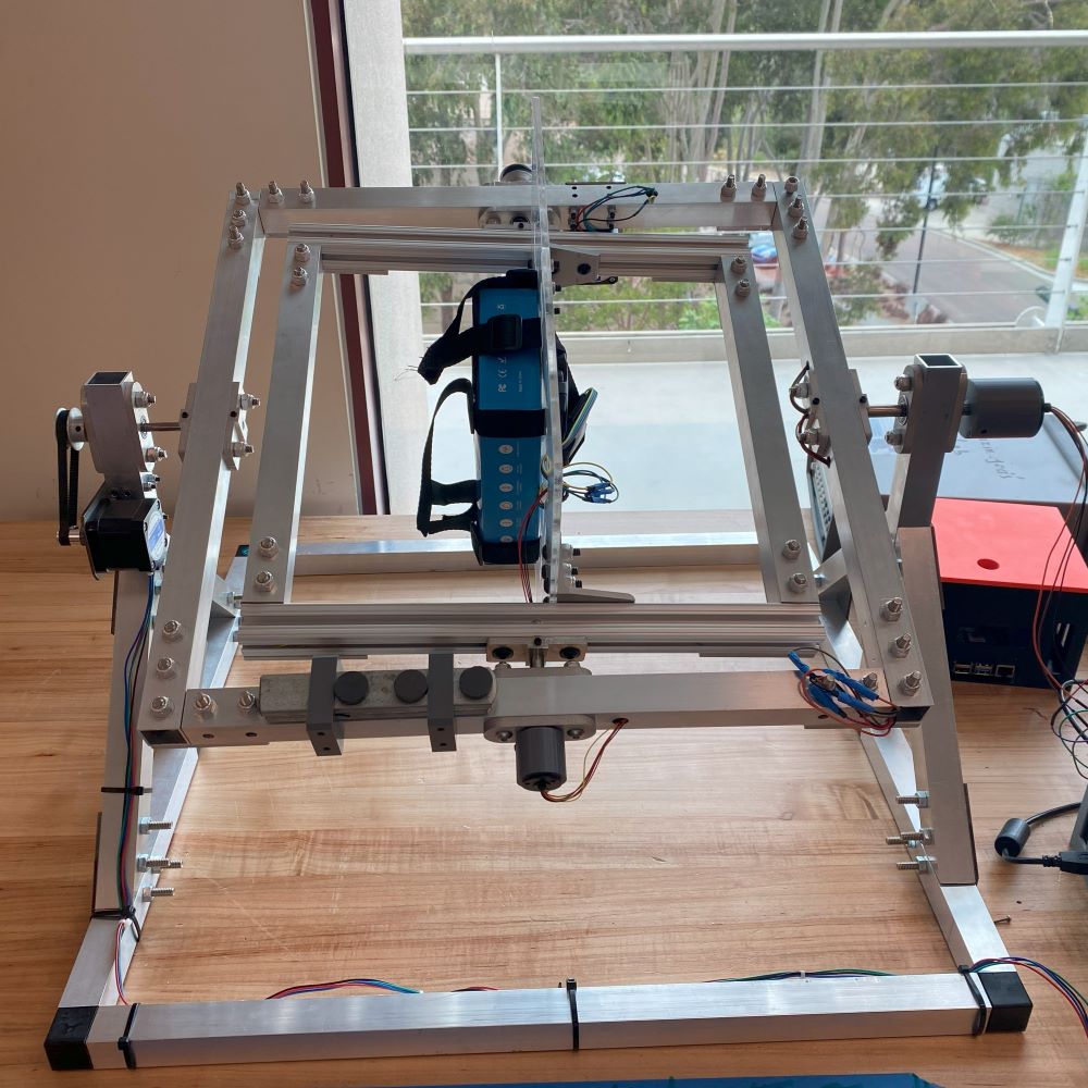 Final design solution of RPM. The design consists of a square nested frame design with an adjustable sample stage mounted in the center. The machine is powered by two stepper motors connected to a pulley system.