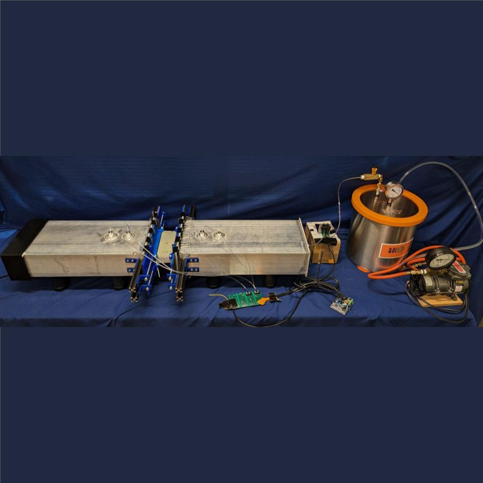 Image of Team 19's project. Two aluminum chambers with a honeycomb panel sample in the middle. Flow control is on the right.